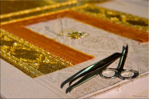 Small scissors and tweezers on an unfinished gold embroidery