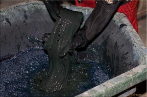 Black rubber gloved hands plunging silk into indigo dye