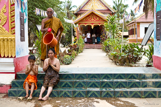 Monk pouring water from a bucket over a praying woman and child, Attapeu Laos