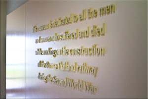 White wall with raised gold tribute to workers on the Death Railway, HellFire Pass