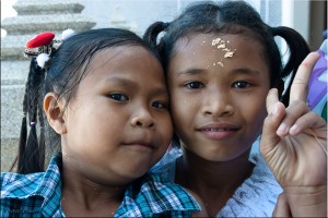 Two young Thai girls with gold leaf on their foreheads smile for the camera.