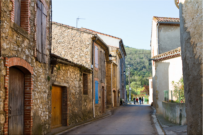 View of a shaded empty street, Granes, with a group of people at the top of it, in the sun.