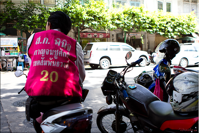 Back of a thai male in a bright pink motorcycle taxi vest