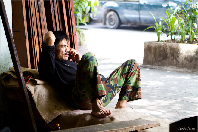Thai man in army pants lying on hessian bags, talking on the phone