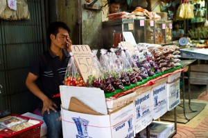 Tired Thai man behind bags of fruit for sale
