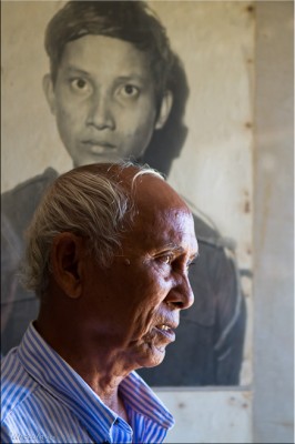 Portrait: Mr Chum Mey, survivor of S-21 Tuol Sleng, in front of a picture of a victim