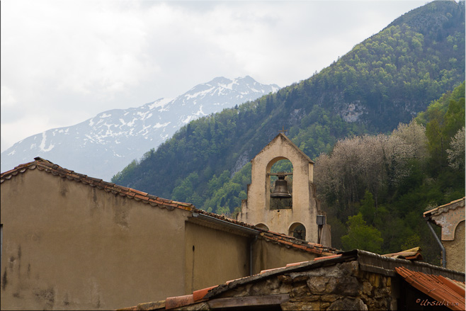 View of church bell, wooded mountain and snow-capped mountain background.