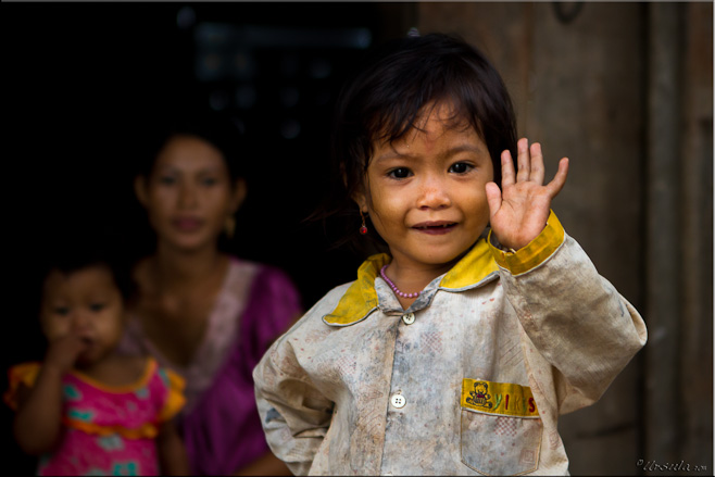 Child in pyjamas waving from a doorway, mum and younger child in shadows behind