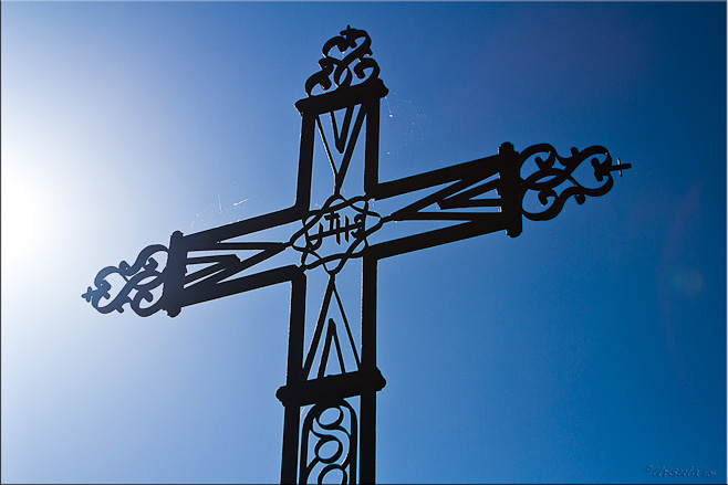 Sun angling into a large black wrought iron cross