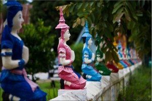 Painted figurines of of kneeling, praying Thai ladies on a white fence