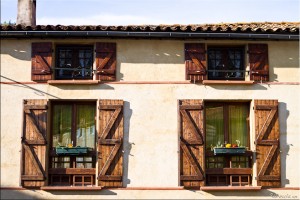 Four windows on the side of a house with their shutters open.