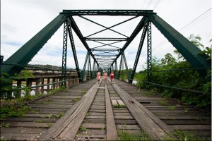 Three thai children walking on a steel-fram bridge with wooden planking
