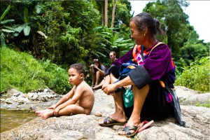 A Lisaw (Lisu) woman in her velvet clothes sits on a rock watching her naked children swimming in a rock-pool.