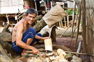 A smiling, squatting Lahu man chops wood
