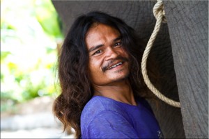 Portrait: A smiling Thai man long hair fixes the rope to an elephant