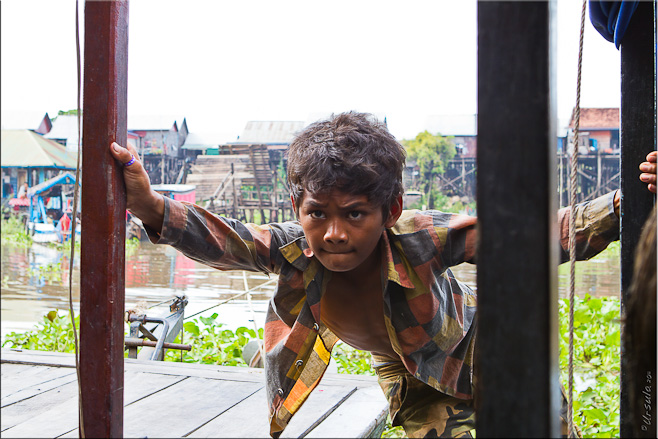 Young khmer male strains to push a large wooden boat away from the dock.