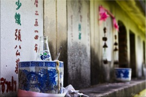 Blue pottery container with a n incense stick and an empty fanta bottle in it: wall of ashes