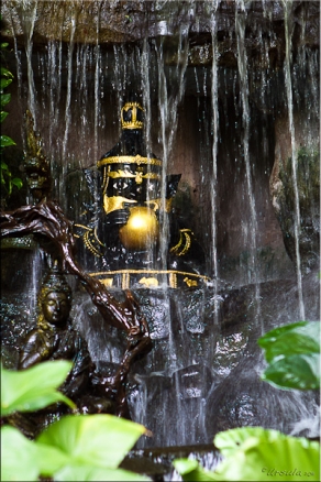 Gold-painted black figurine of a Thai hermit, set in a waterfall