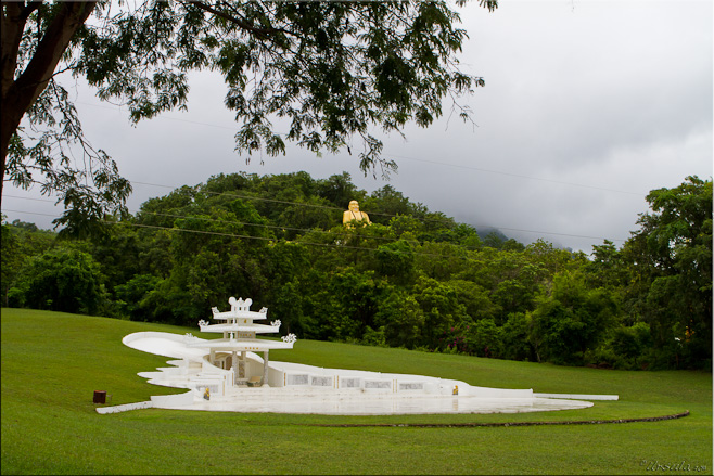 An elaborate white chinese grave, set into a sculptured green lawn - a golden Chinese buddha on the green hill behind