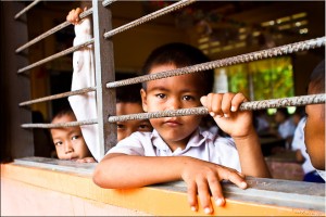 Three young boys look out the barred window of their Khmer classroom