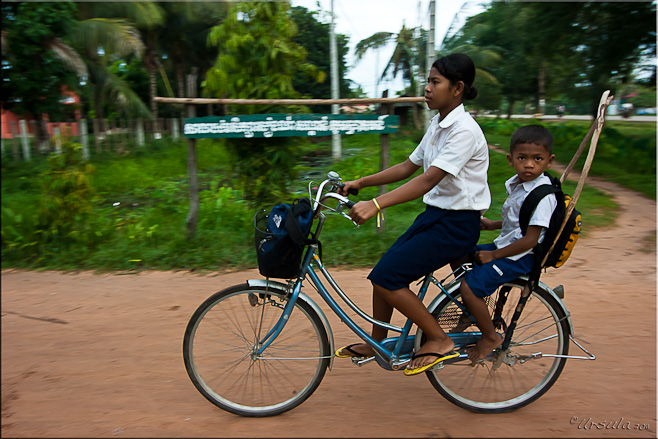 Teenage girl in uniform on a bicycle, pedalling her younger brother into Sandan School, Cambodia