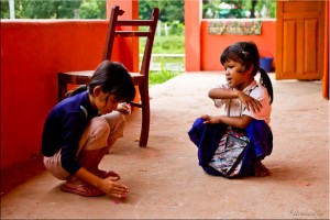 Two young khmer girls squatting to play a game like jacks.