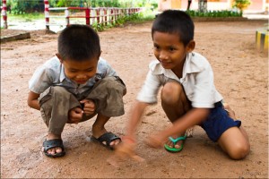 Two khmer boys squatting on dirt, playing marbles