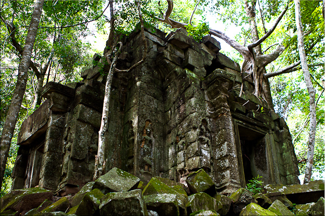 A pile of mossy rocks around the ruins of a 12th century Khmer temple.