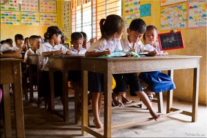 Khmer children at wooden desks writing on personal chalkboards.