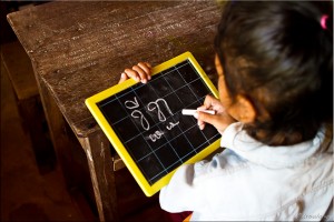 Khmer girl writing letters on a personal chalkboard.