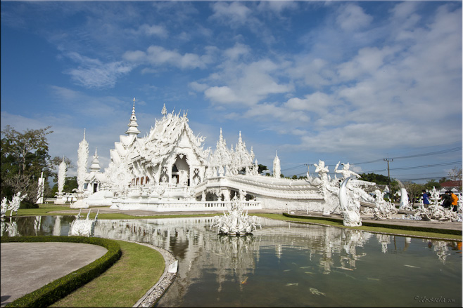 Wide angle view of the white temple: Wat Rong Khun set in waters an gardens.