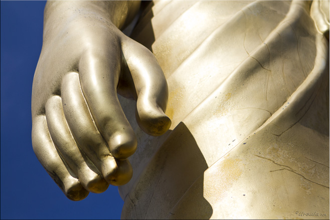 Large hand at the side of a golden buddha statue.