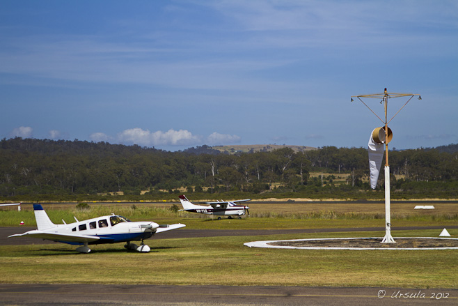 Two small propellor planes parked on grass; wind vane with low wind.