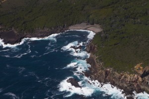 Aerial view: white waters crashing onto red cliffs.