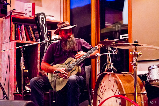 Bearded male in a felt cowboy hat playing a steel guitar.