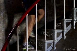 Man's legs in running shoes climbing up a wrought iron circular stairway.