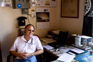 Man in a white shirt and tinted glasses sitting at a busy desk.