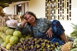 A middle-aged Khmer woman reclining on a table covered in mangosteen, pomelo and pineapple.