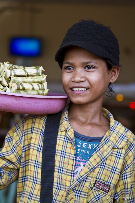 Portrait: Young khmer girl in a wool cap and plaid shirt selling bamboo-wrapped treats.
