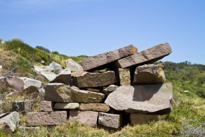 Rough pile of pink Gabo granite against green grass and blue sky.