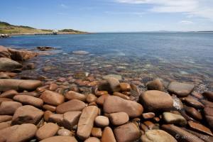 Rounded boulders of granite at a blue shoreline.