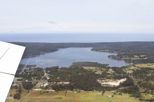 Aerial view: lake surrounded by green lands, ocean behind.