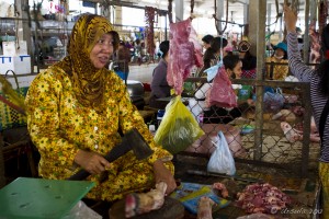 Woman in yellow head-scarf cutting a leg of meat in a Cambodian market.