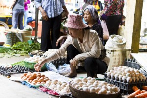 Woman squatting in a Khmer market selling fresh eggs.