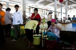 Busy Battambang market scene, with a woman buying garlands from a flower seller.