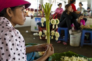 Portrait: profile of a khmer woman in a red hat making jasmine garlands