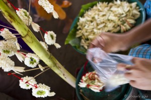 Jasmine garlands hanging and woman's hands making them.