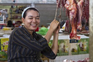 Portrait: Cambodian woman smiling next to hanging meat.