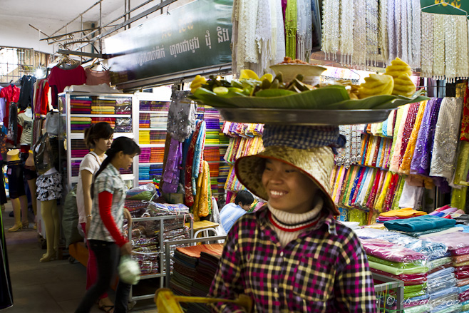 Cambodian woman in a straw hat with a fruit platter on her head.