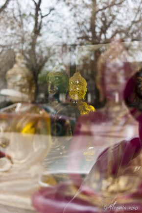 Reflections of trees and coloured glass Buddha images, shop window: Luang Prabang